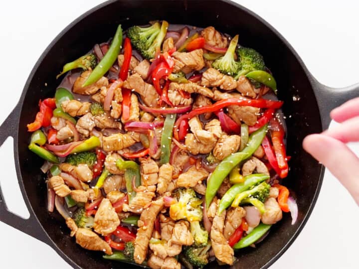 Sprinkling the stir-fry with sesame seeds.