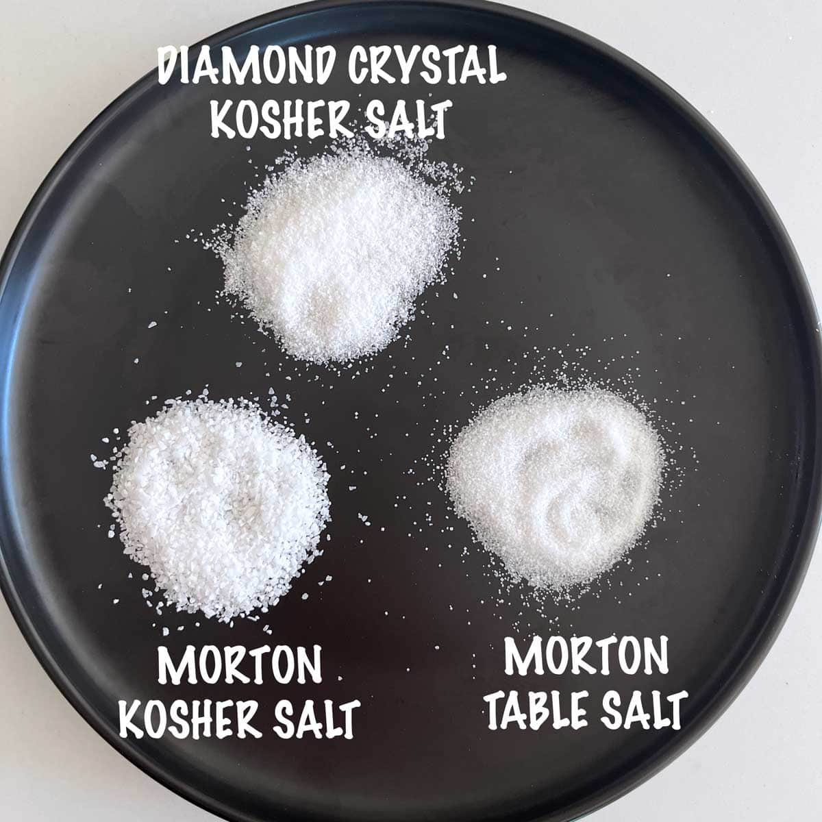 Three mounds of salt on a black plate for comparison: Diamond Crystal, Morton kosher salt, and Morton table salt.