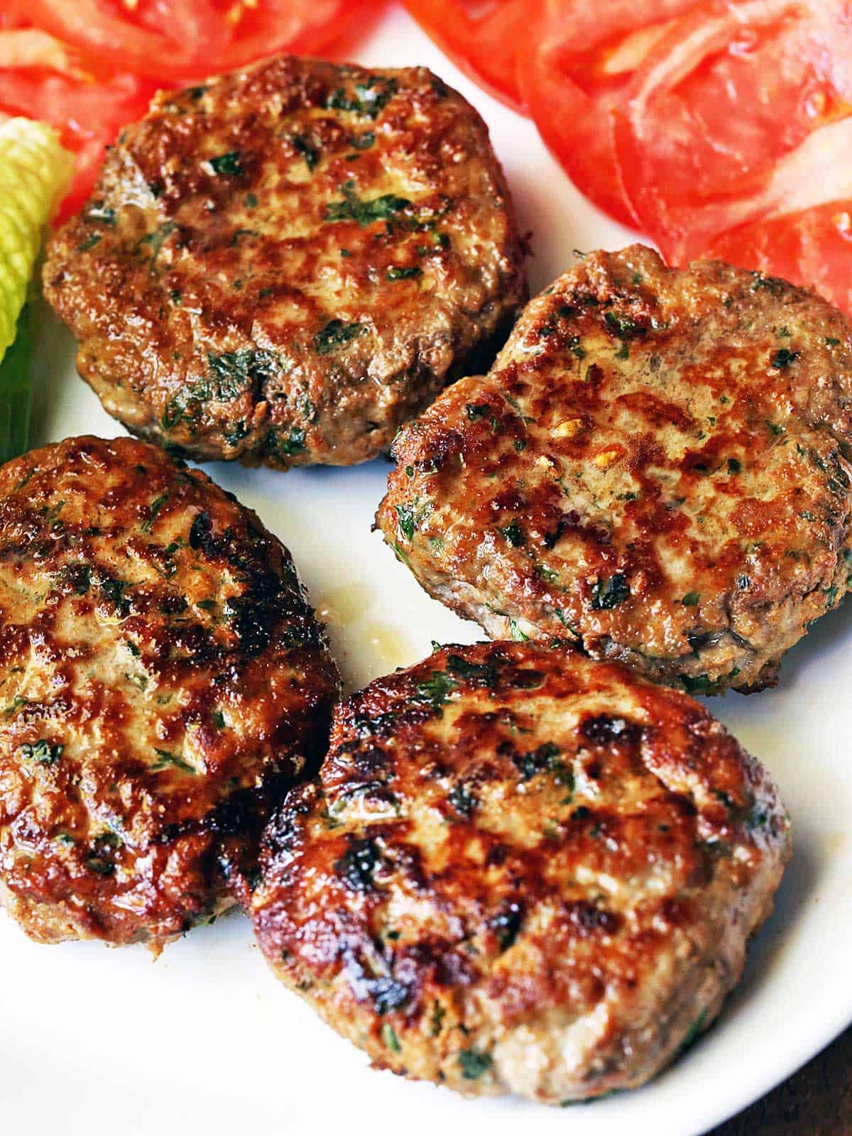 Turkey burgers are served on a white plate with lettuce and tomatoes.