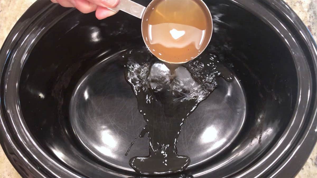 Adding broth to slow cooker pan.