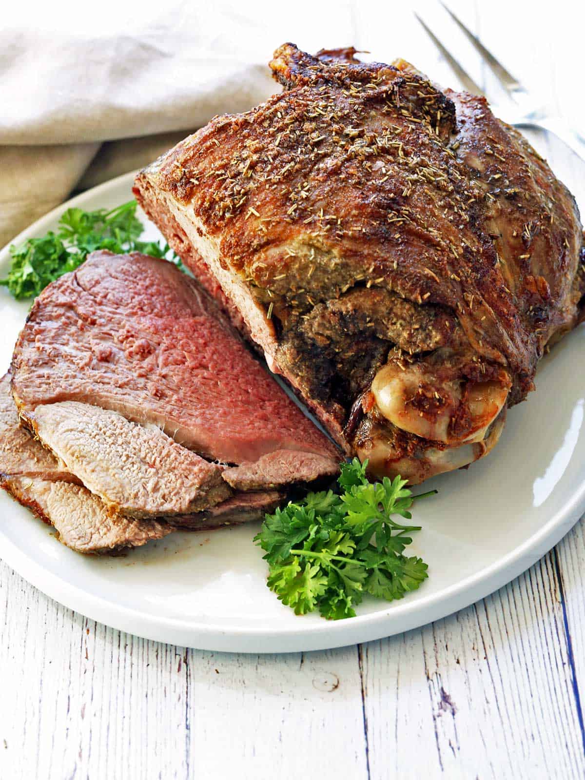 A roasted leg of lamb is served on a white platter, garnished with parsley.