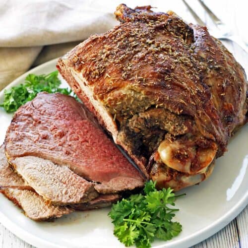 A roasted leg of lamb, sliced, is served on a white plate.
