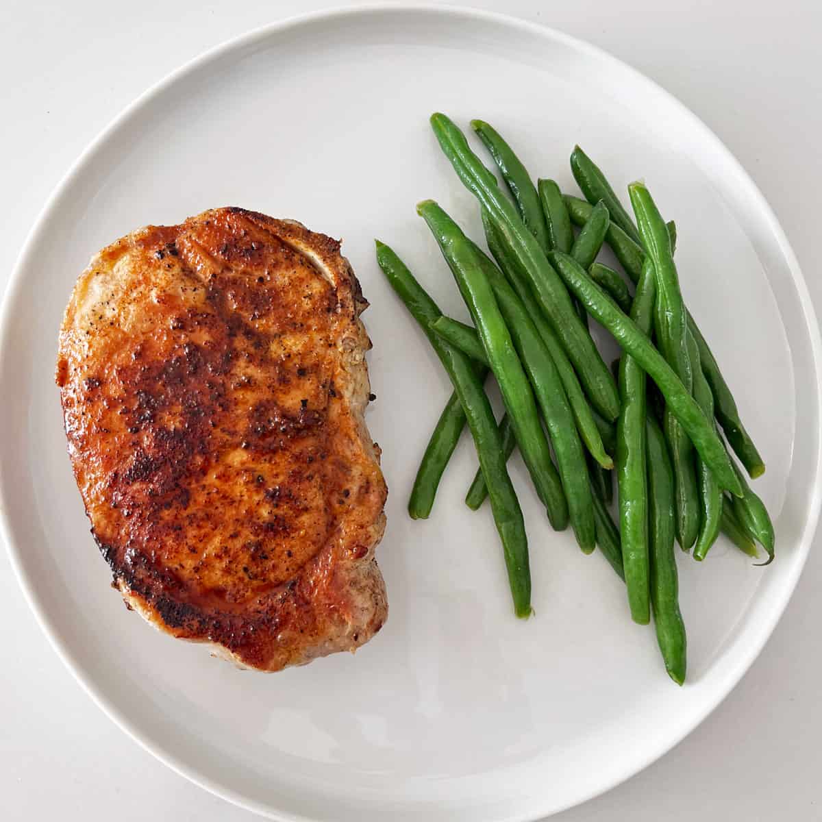 A pork chop is served with green beans.