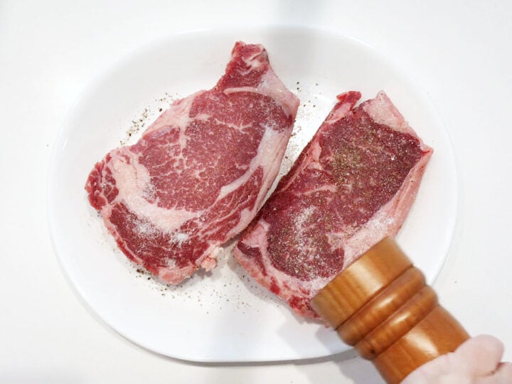 Seasoning the steaks with freshly ground black pepper.