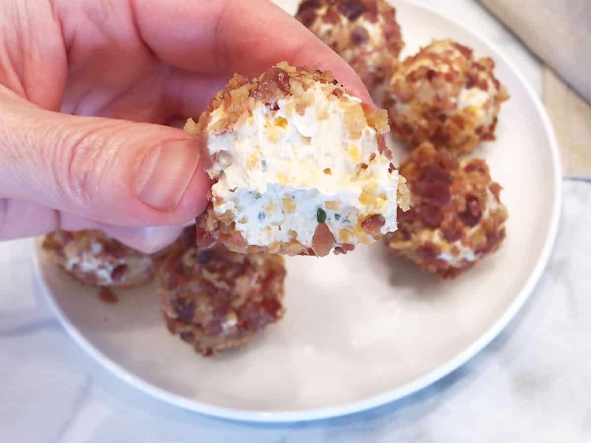 A hand is holding a cheese ball with a bite.