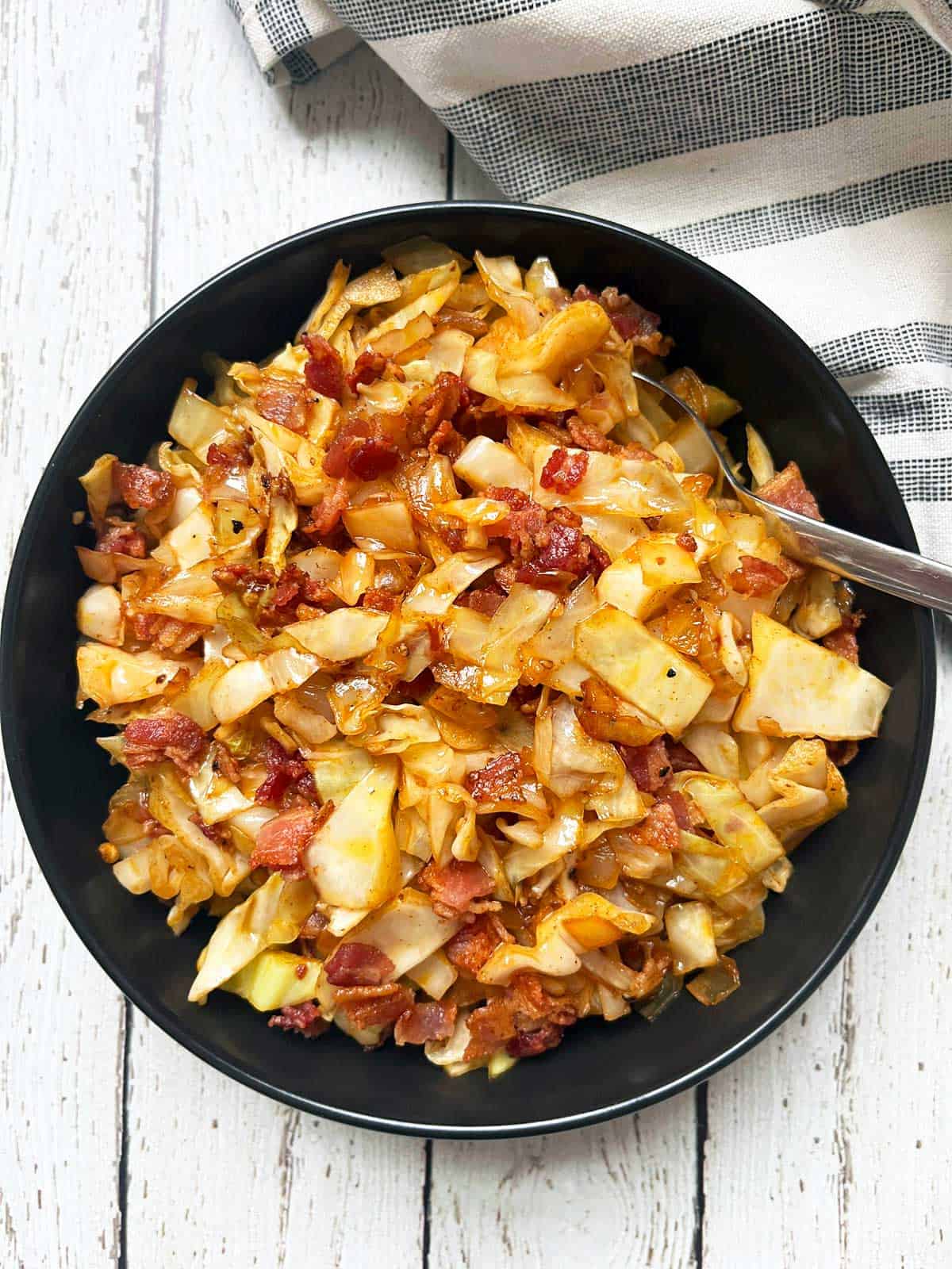 Fried cabbage is served in a dark bowl with a napkin.