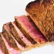 London broil steak is sliced and served on a white cutting board.