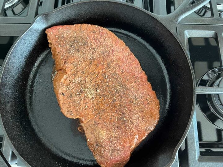 Cooking the London broil on the first side on a cast-iron skillet.
