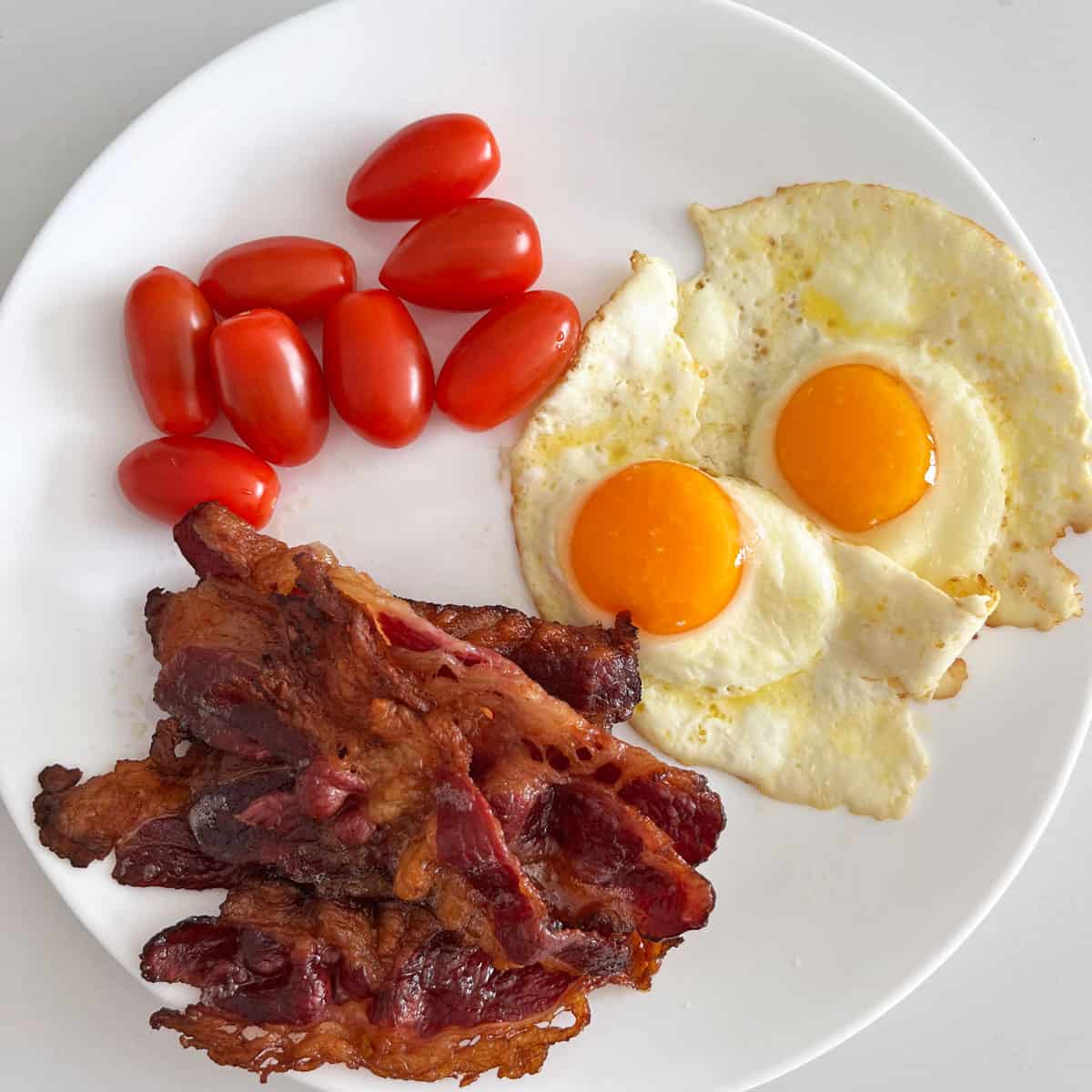 Beef bacon is served with eggs and tomatoes.