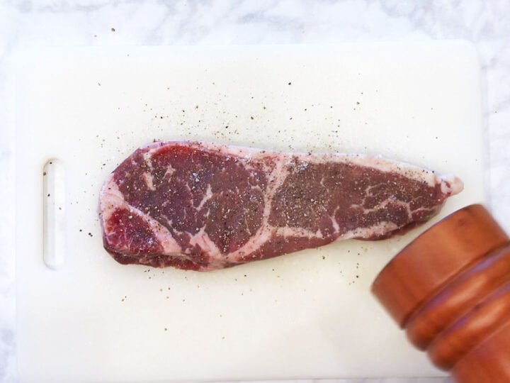 Seasoning a steak with salt and pepper.