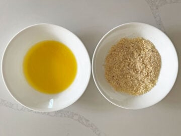 A bowl with melted butter and a bowl of seasoned parmesan.