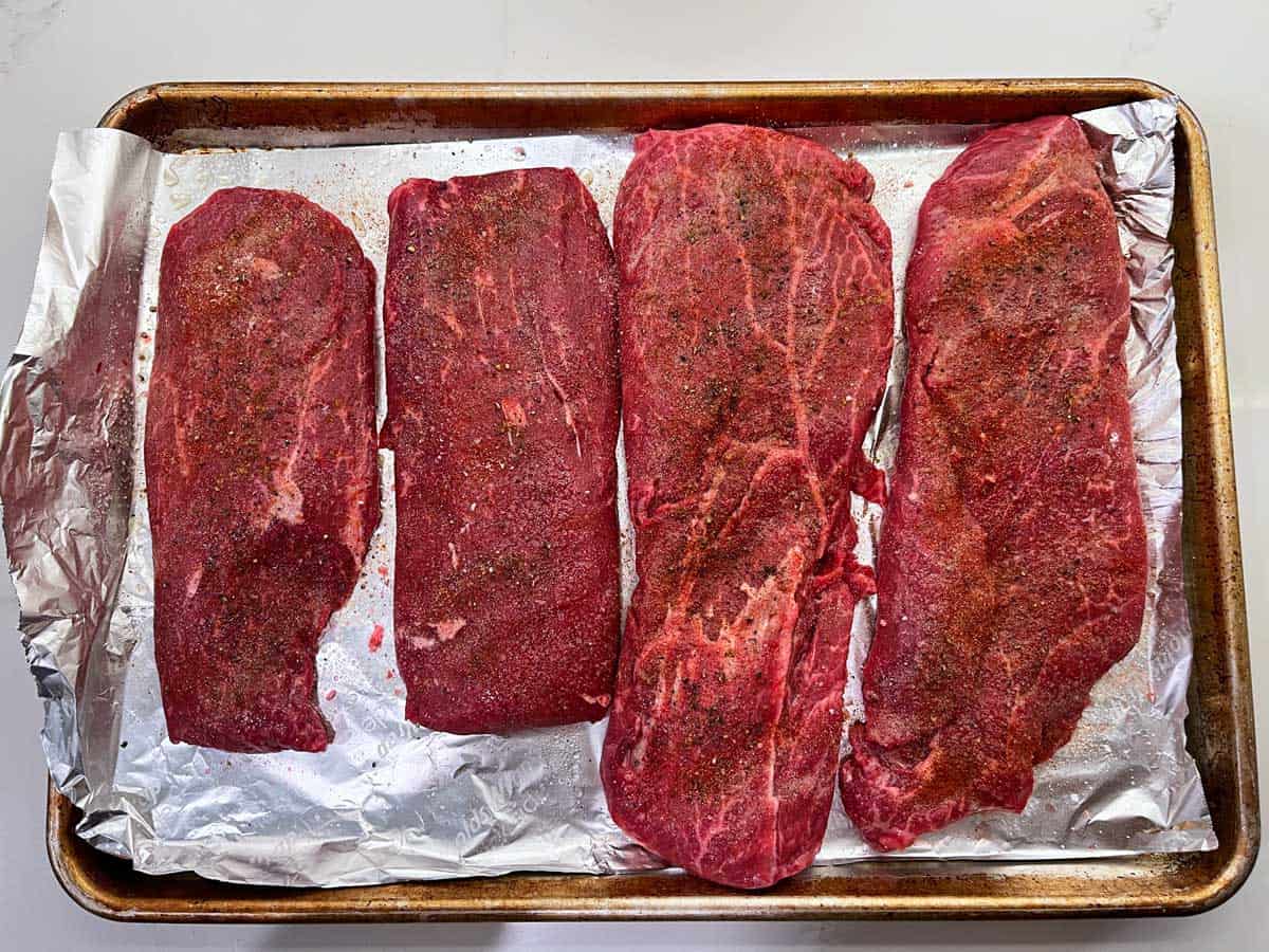 Four flat iron steaks on a baking sheet.