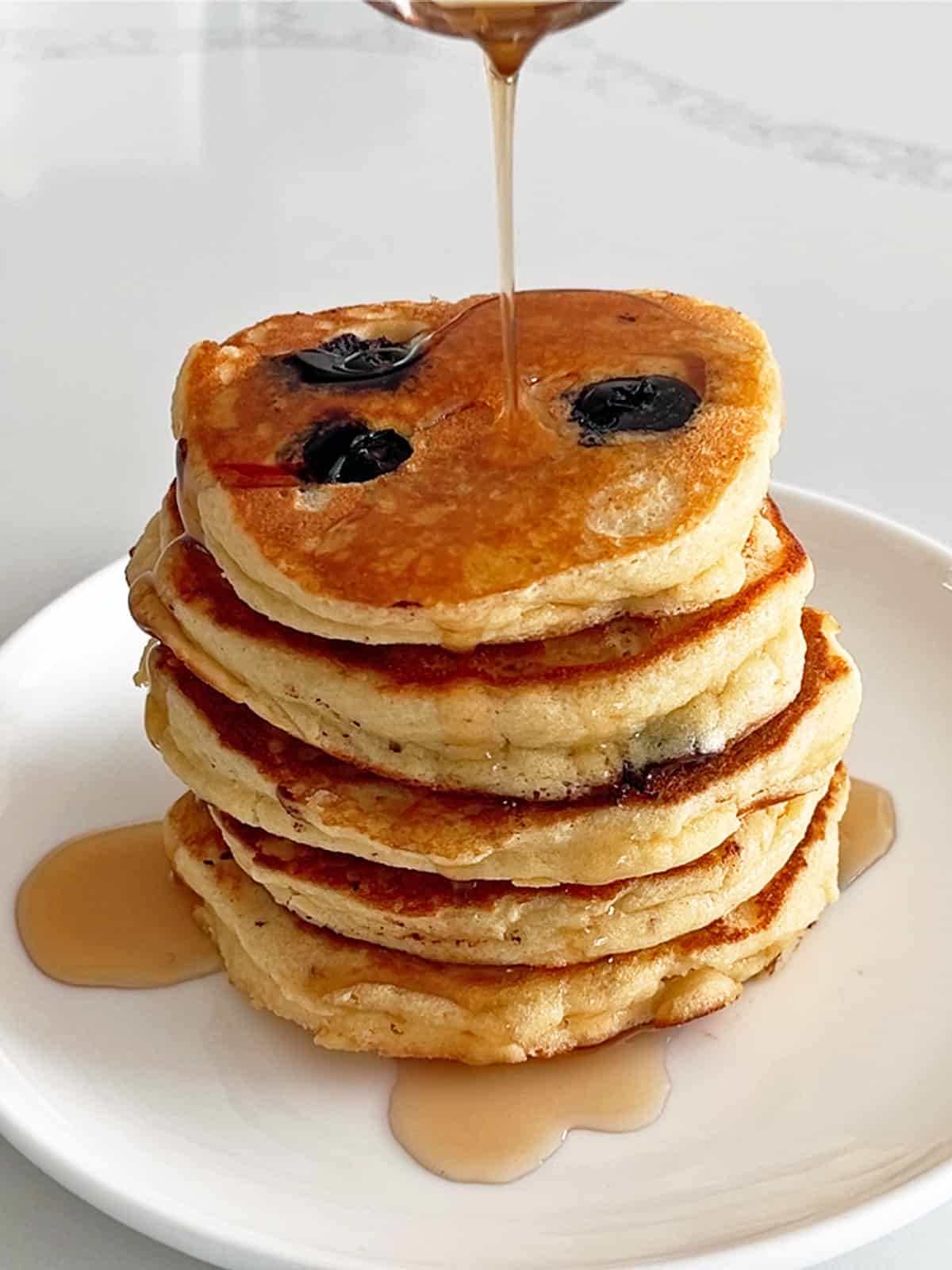 Pouring maple syrup on the pancakes.