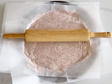 Using a rolling pin to spread the crust mixture on the pan.