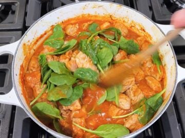 Mixing spinach leaves into the pork stew.