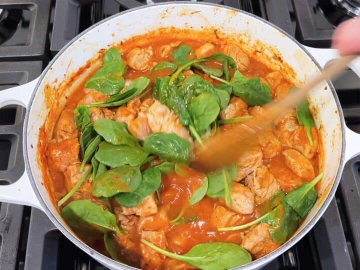 Mixing spinach leaves into the pork stew.