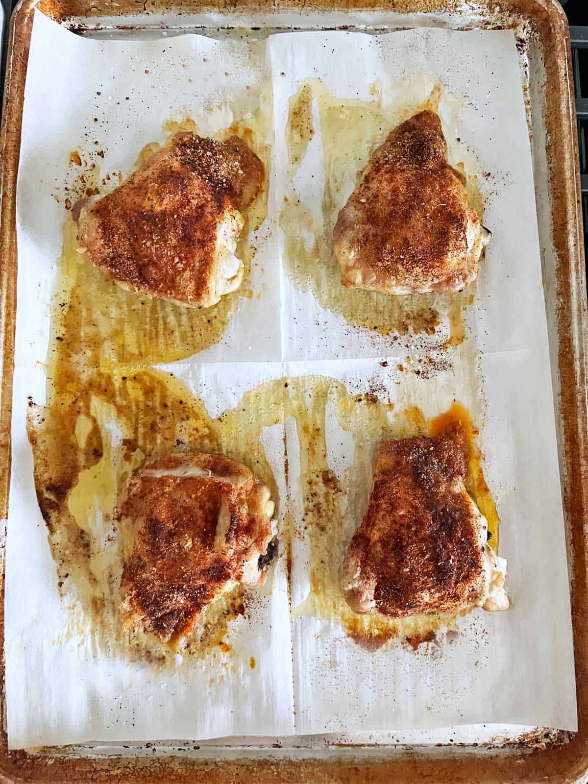 Four crispy chicken thighs are ready on the baking sheet.
