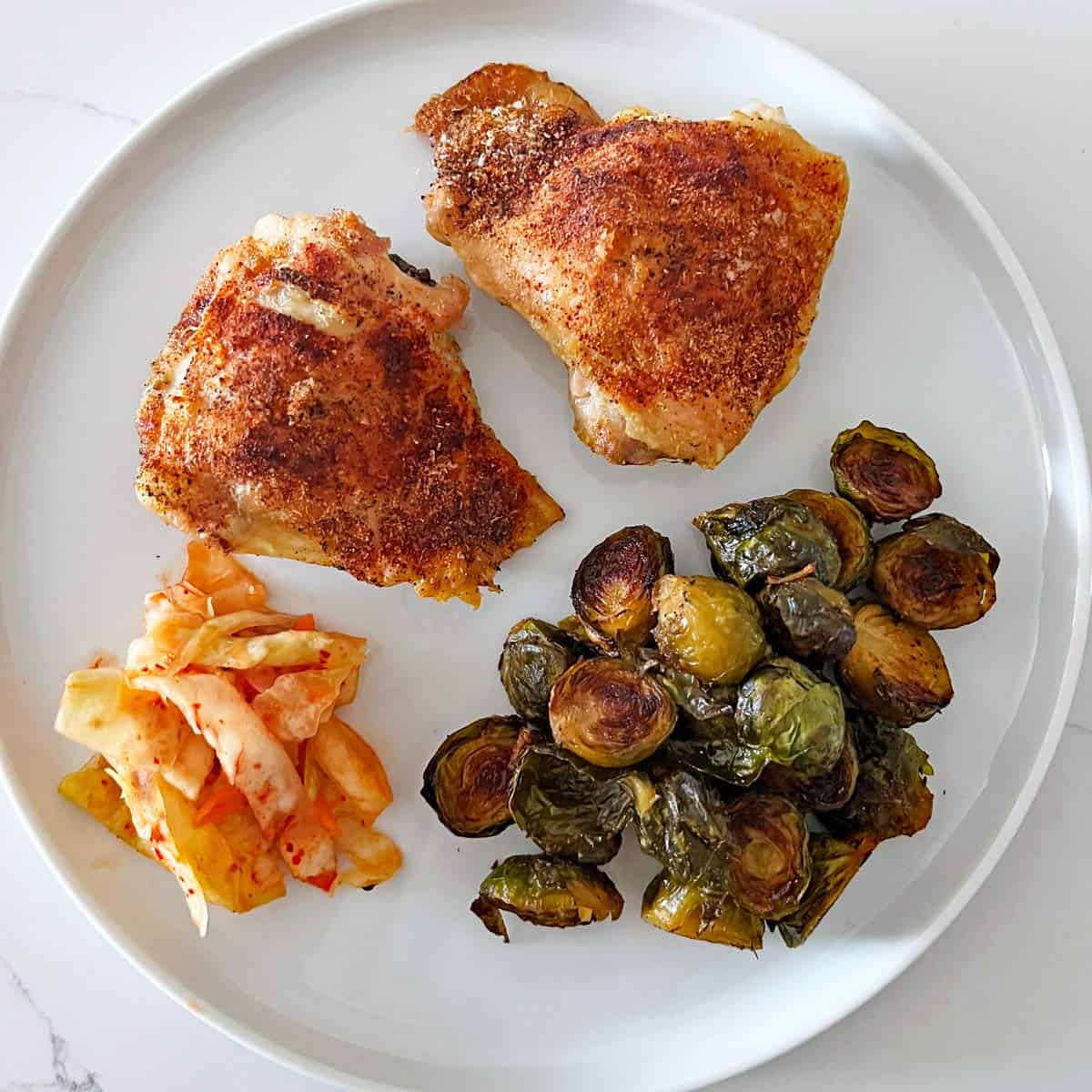 Two crispy chicken thighs are served with roasted Brussels sprouts and kimchi.