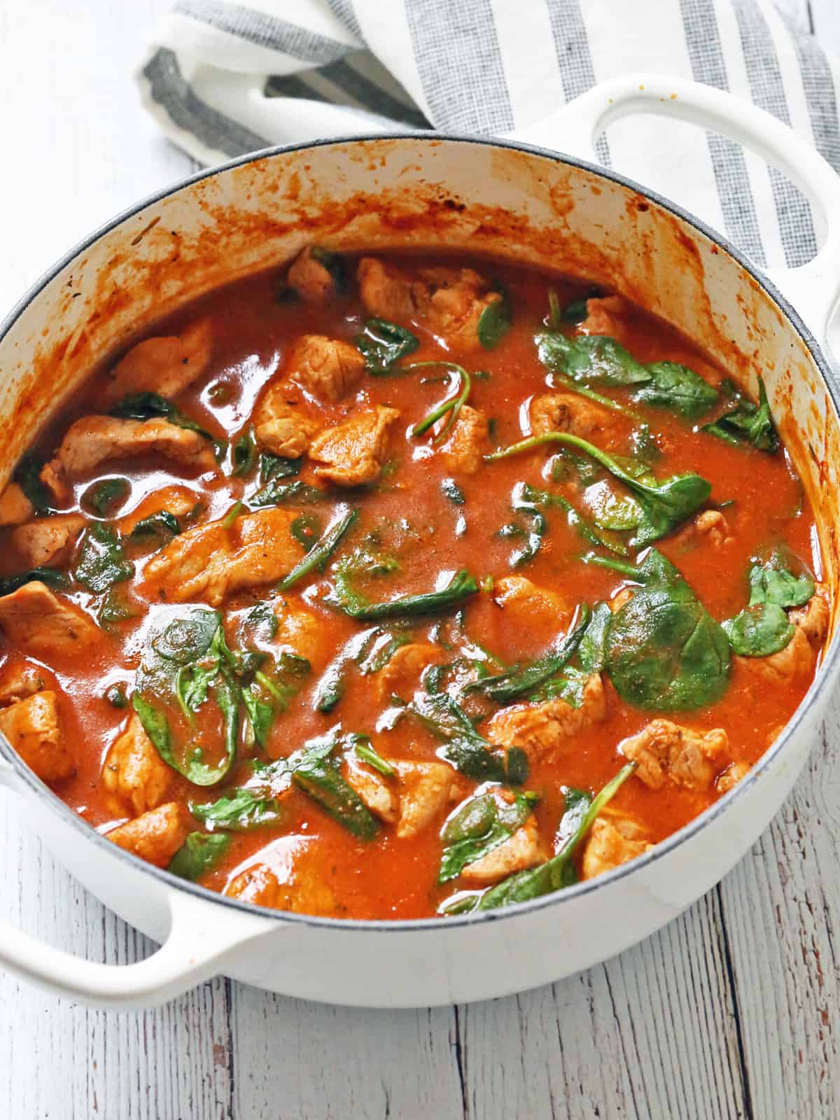 A pork stew is served in a white saucepan.