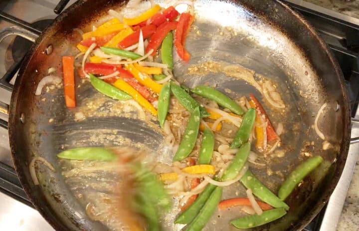 Adding garlic, ginger, and snow peas to the skillet.