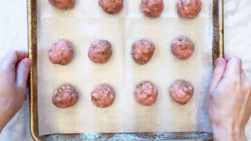 The raw meatballs are arranged in a pan.