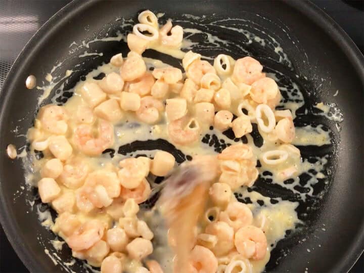 Adding back the seafood to the skillet and mixing it with the sauce.