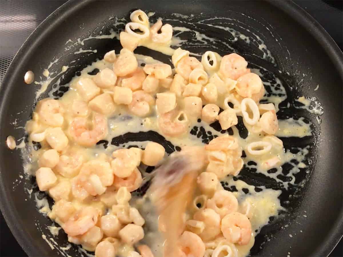 Adding back the seafood to the skillet and mixing it with the sauce.