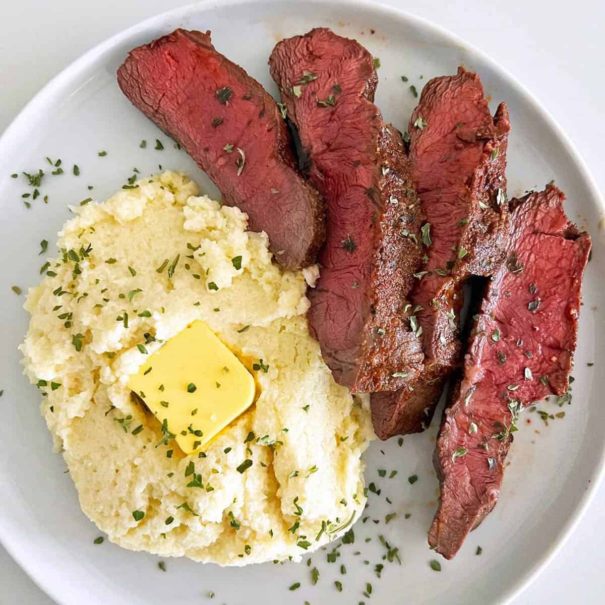Flat iron steak is served with a side of mashed cauliflower.