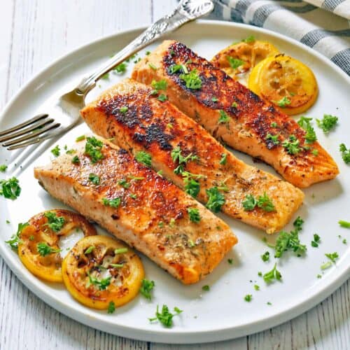 Pan fried salmon is served on a white plate.