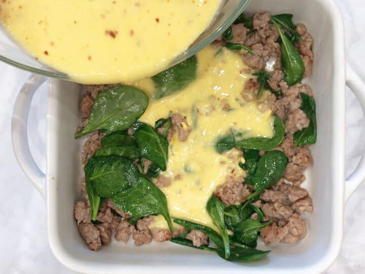 Pouring the egg mixture on top of the sausage and spinach.