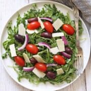 Arugula salad is served on a white plate.
