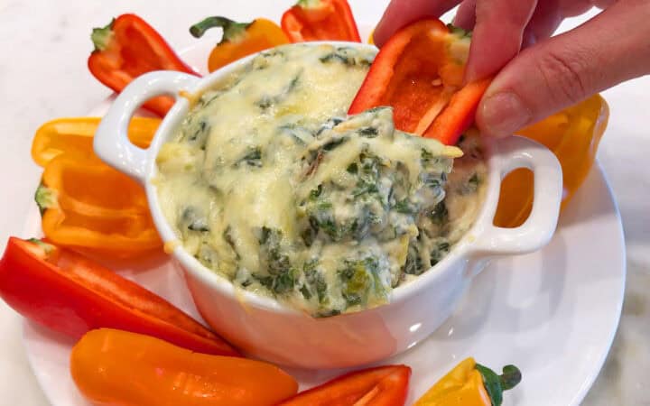 Spinach artichoke dip is served with mini peppers.
