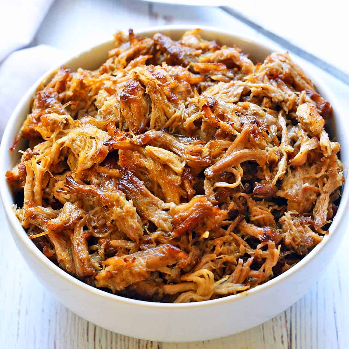 Slow cooker carnitas are served in a white bowl.