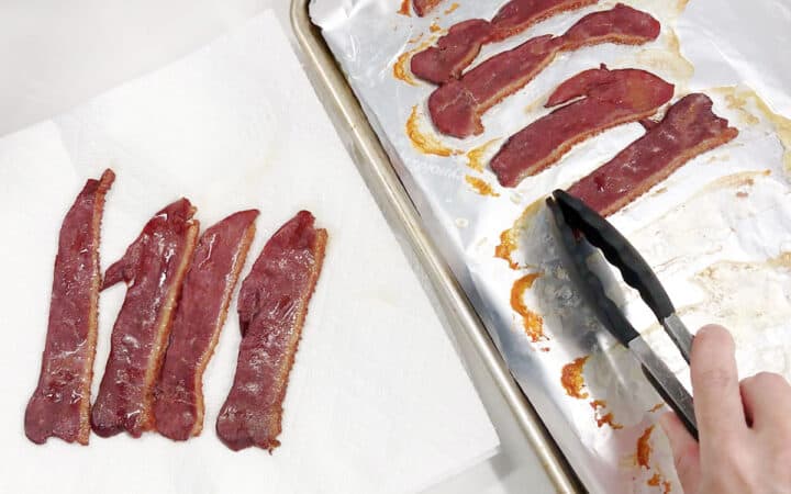Placing the cooked bacon on paper towels to drain.