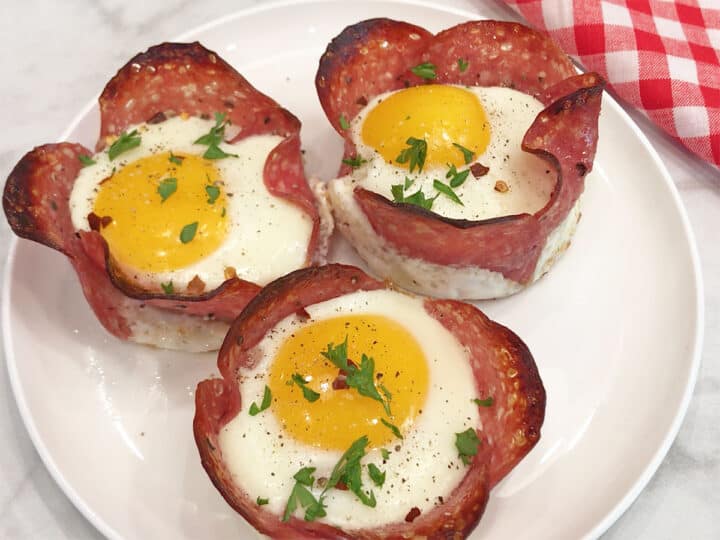 Salami and egg cups are served on a white plate.