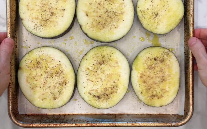 Oiled and seasoned eggplant slices on a baking sheet.