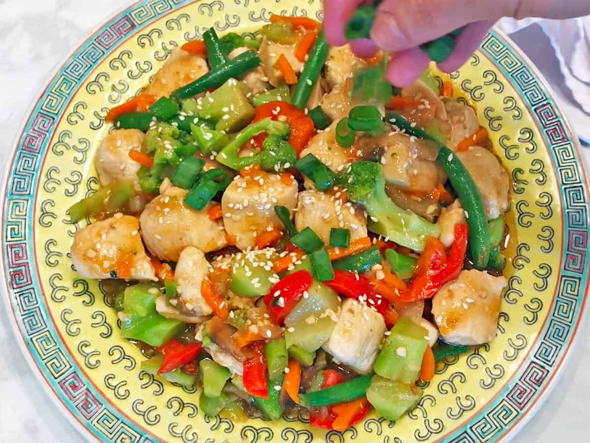 Garnishing the stir-fry with chopped scallions.