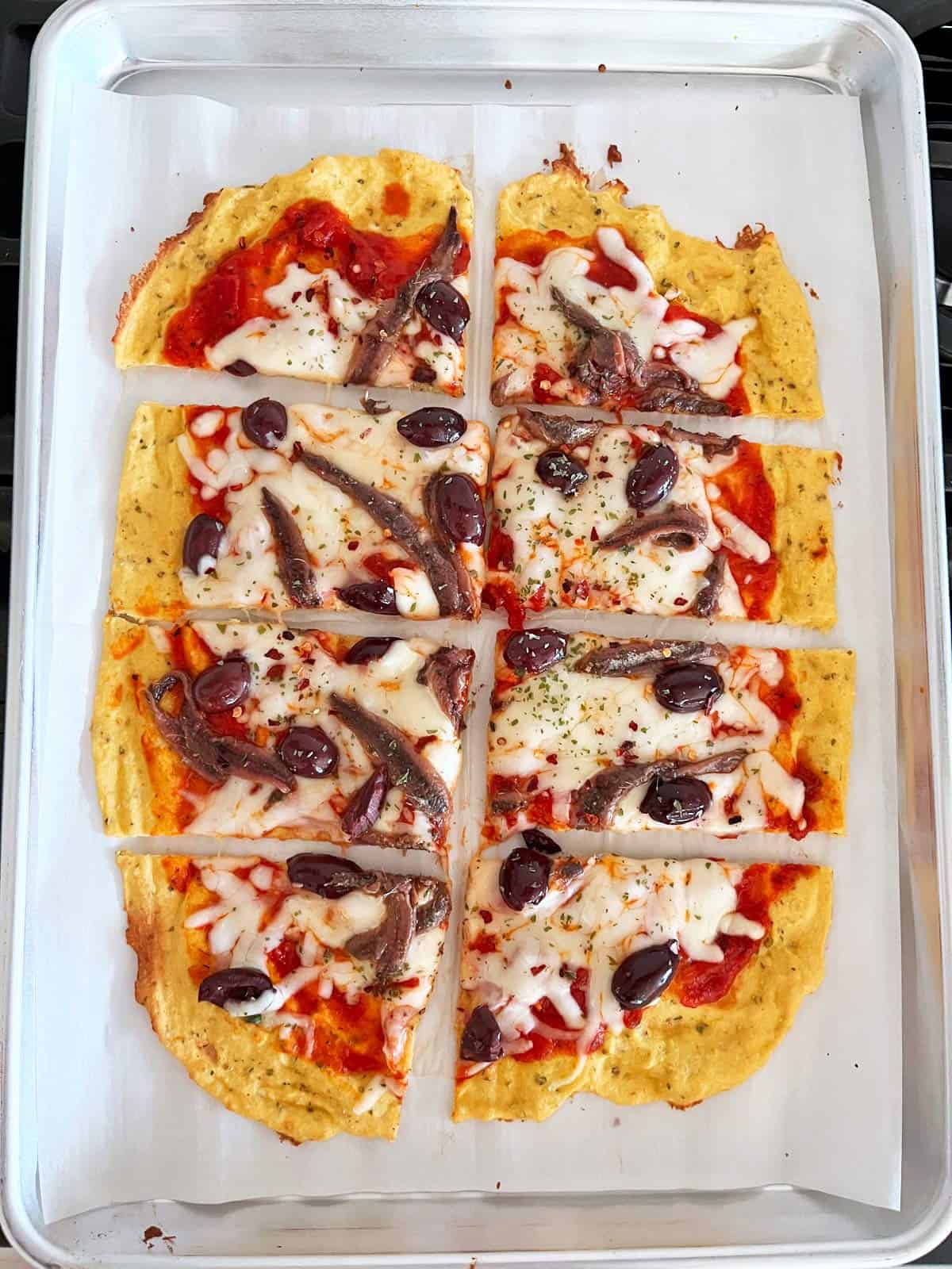 Sheet pan coconut flour pizza crust is topped with olives and anchovies.