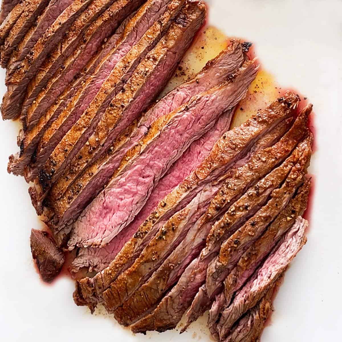 Broiled flank steak is served on a white cutting board.