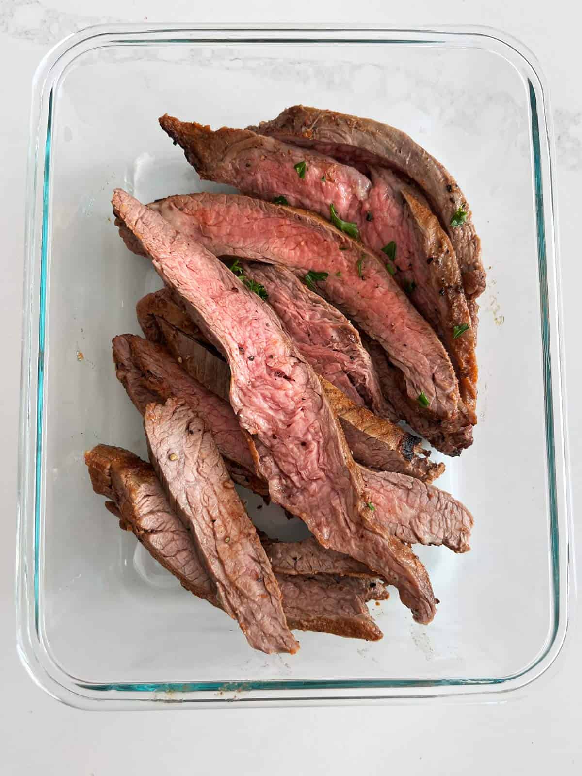 Leftover flank steak slices are stored in a glass food storage container.