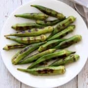 Grilled okra is served on a white plate with a napkin.