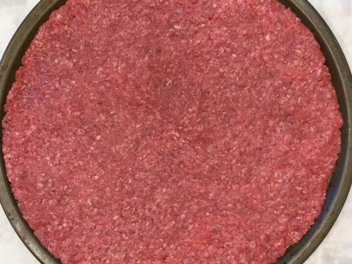 The ground beef covers a pizza pan.