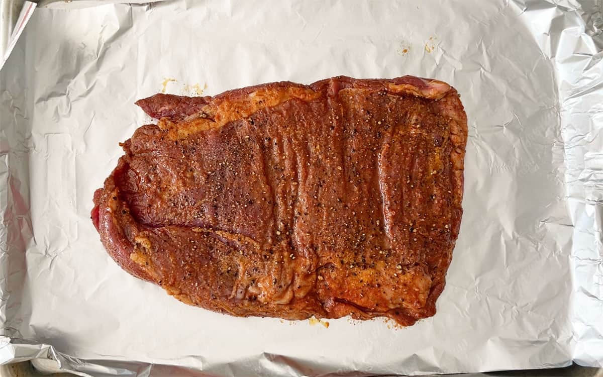 The marinated and seasoned steak was placed on a baking sheet.