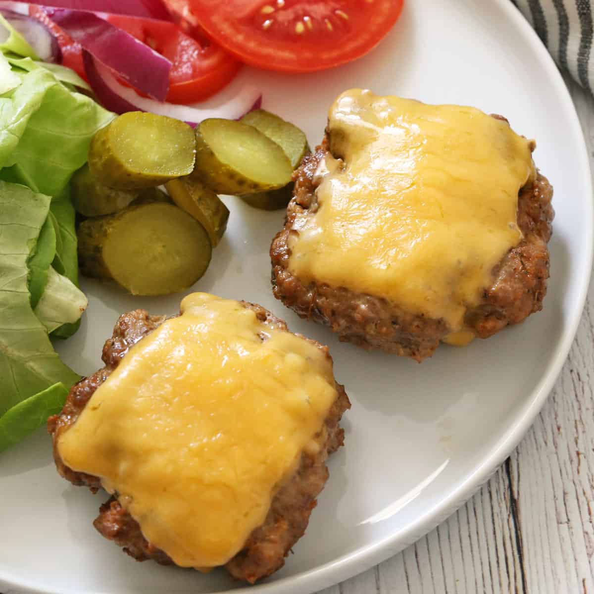 Two pork burgers are topped with melted cheese.