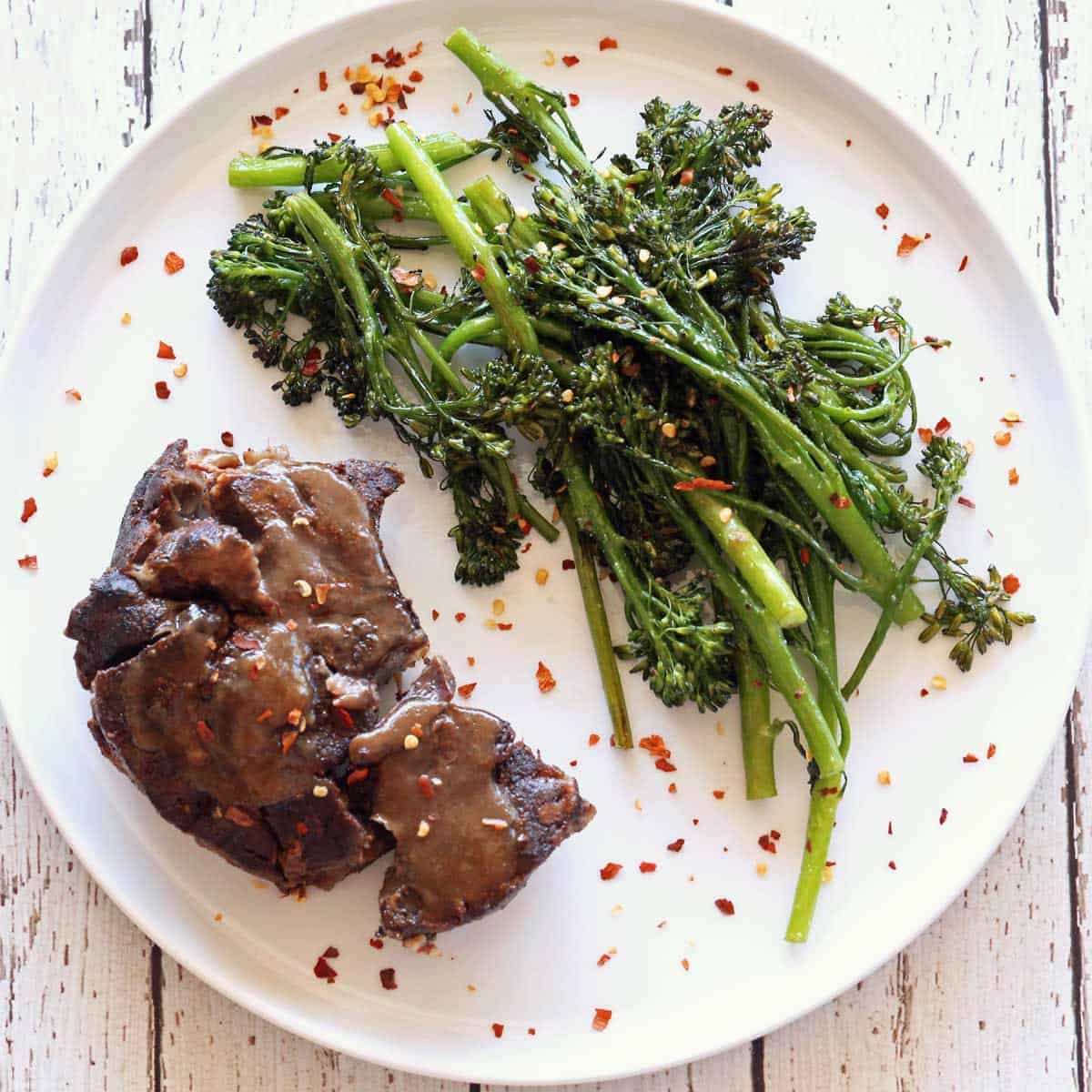 A beef shank and roasted broccolini on a plate.