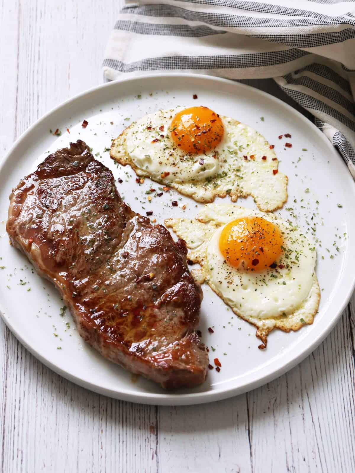 Steak and eggs are served on a white plate.