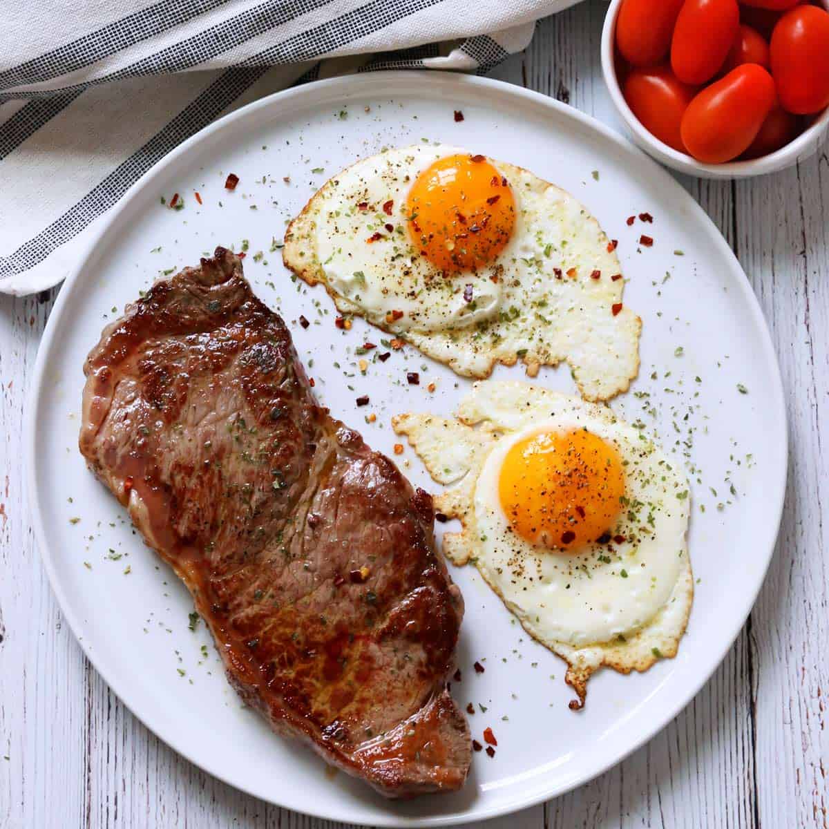 Steak and eggs are served with cherry tomatoes.
