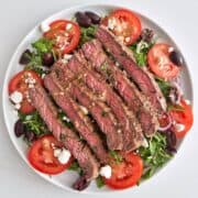 A steak salad is served on a white plate.