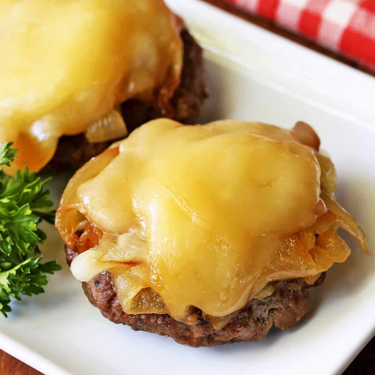 Broiled burgers with onions and cheese are served on a white plate.