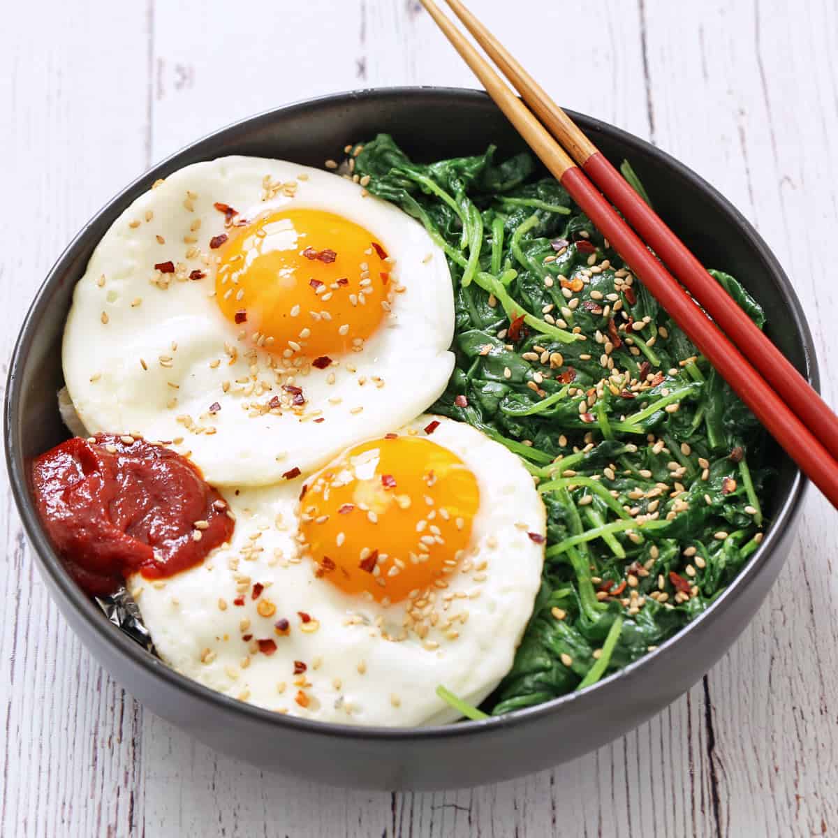 A sauteed kale bowl with fried eggs and Gochujang.